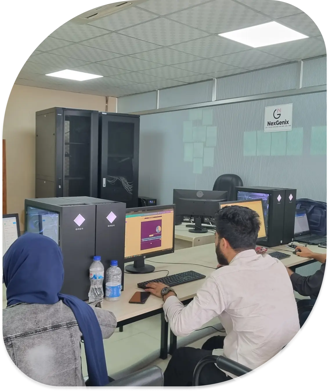 People working on desktop computers in an office with NexGenix branding on the wall